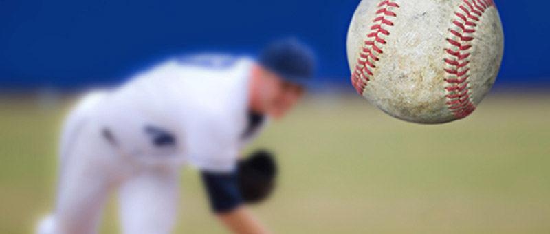 close up of a baseball with a blurred pitcher in the background