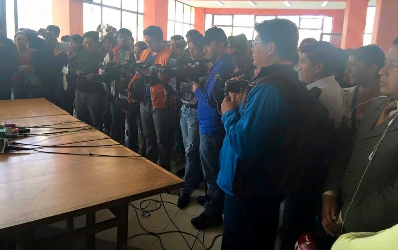 a group of journalists standing around a wooden table