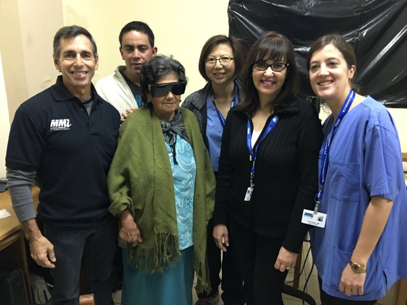 five medical staff standing around an old woman wearing dark glasses