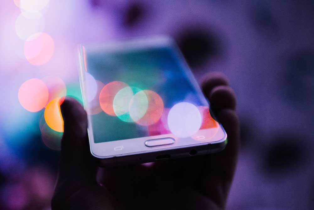 hand holding smart phone with bokeh lights along the surface and background